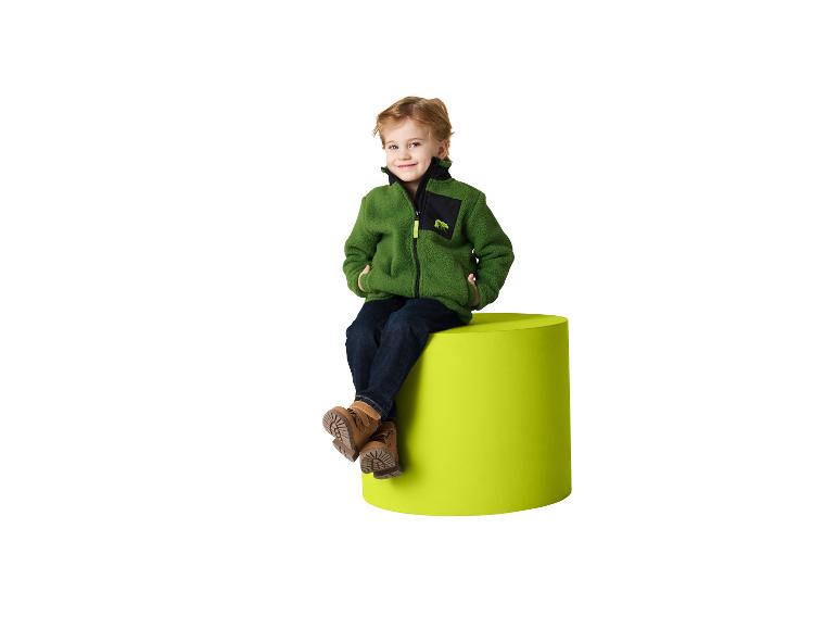 Garçon en veste polaire verte et jean, assis sur un pouf vert citron.