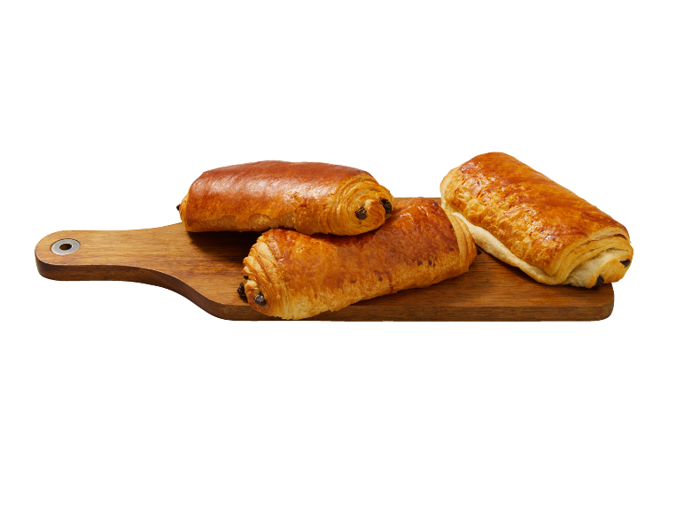 Trois pains au chocolat dorés sur une planche à découper en bois.