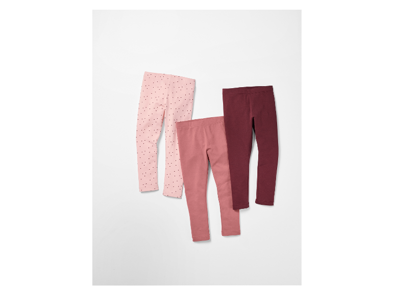 Trois leggings pour enfants dans des tons rose et bordeaux.