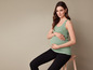 Une femme enceinte portant un débardeur vert et un pantalon noir.