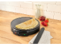 Crêpière avec crêpes, lait, confiture et fraises sur un comptoir en bois.
