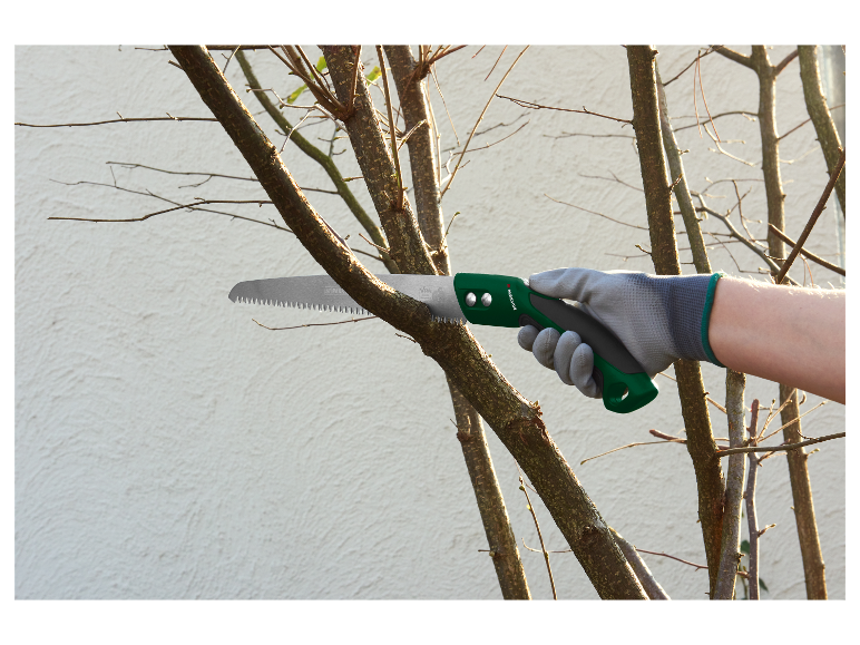 Une main gantée utilise une scie à main Parkside pour tailler un arbre.