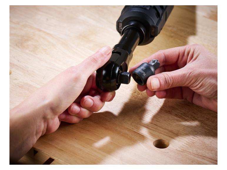 Mains fixant un adaptateur de douille à une clé à cliquet sur un établi en bois.