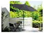 Un parasol gris avec un socle en pierre, une table et des chaises noires sur une terrasse.