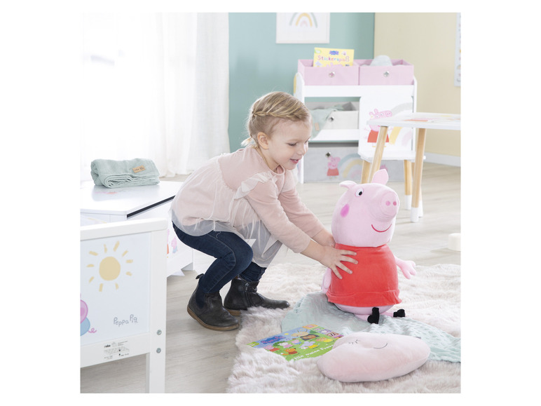 Une fillette joue avec une peluche Peppa Pig et un livre.