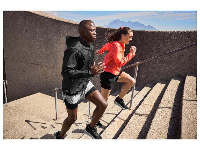 Deux personnes en tenue de sport montent des escaliers extérieurs, avec des montagnes en arrière-plan.