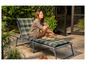 Une femme assise sur une chaise longue à carreaux verts dans un jardin.