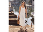 Une femme en robe blanche et en sandales marche le long d'un port avec un sac en osier.