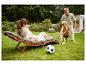 Femme se relaxant sur une chaise longue de jardin pendant qu'un homme et un enfant jouent au football.