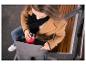 Femme mettant une tasse de voyage rouge dans un sac à dos gris sur un banc.