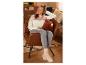 Une femme en pull blanc assise dans un fauteuil marron.
