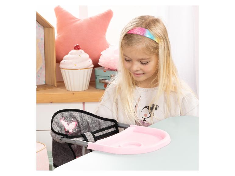 Une enfant assise sur une chaise haute rose avec un motif papillon et un plateau rose sur une table.