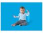 Bébé souriant en body bleu et pantalon gris, assis avec un jouet bleu.