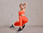 Femme en leggings et soutien-gorge de sport orange avec des haltères.