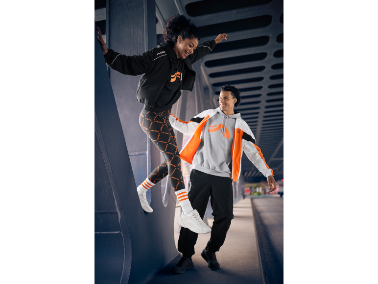 Deux personnes en tenue de sport, leggings noirs et oranges, sweats à capuche et vestes, en milieu urbain.