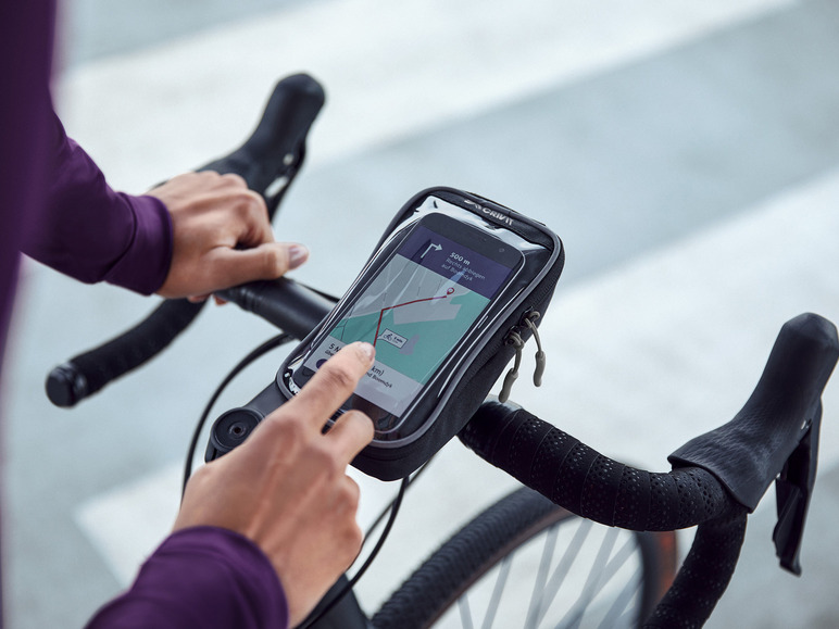 Une main utilise un smartphone dans un support de téléphone Crivit sur le guidon d'un vélo.