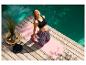 Femme faisant du yoga sur un tapis rose près d'une terrasse en bois et d'une piscine.