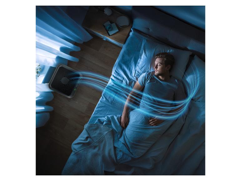 Purificateur d'air soufflant de l'air frais sur un homme endormi dans une pièce sombre.