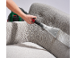 Nettoyeur de tissus d'ameublement nettoyant un canapé gris avec un accessoire de nettoyage.