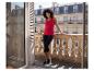 Femme en débardeur rouge et legging capri noir sur un balcon avec balustrade en pierre.