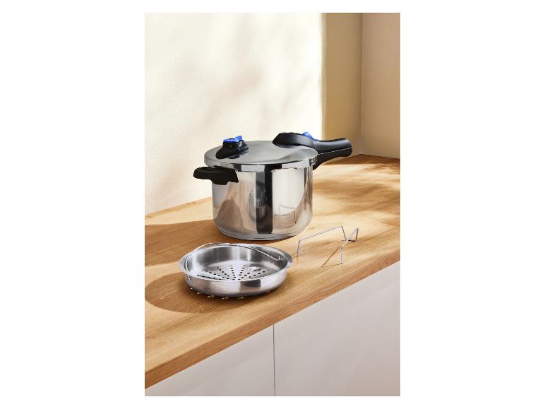 Une cocotte-minute en acier inoxydable et un panier vapeur sur un comptoir en bois.