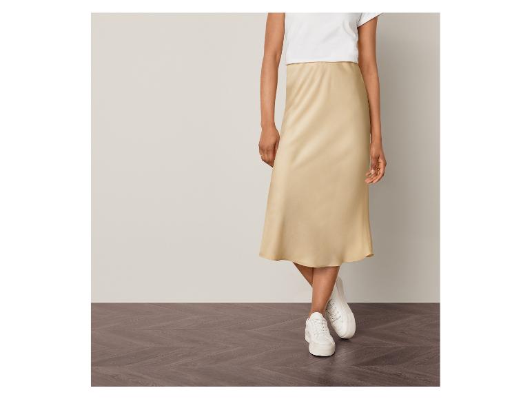 Une femme porte une jupe en satin beige et des baskets blanches.