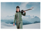 Une fille vêtue d'une tenue de ski verte avec des skis sur l'épaule.
