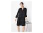 Femme en mini-robe noire à volants et manches longues, debout à côté d'une chaise en métal.
