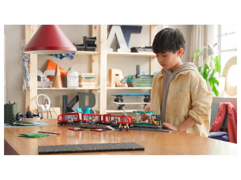 Un enfant joue avec un train et une gare LEGO City sur une table en bois.