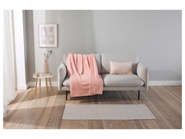 Plaid rose poudré sur un canapé gris clair, avec coussin assorti et tapis beige.