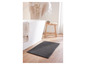 Un tapis de bain gris dans une salle de bain avec une baignoire et un tabouret en bois.