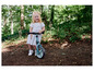 Une petite fille fait du vélo sans pédales bleu Hudora dans la forêt.