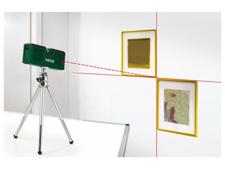 Niveau laser sur trépied projetant des lignes rouges sur un mur avec des cadres.