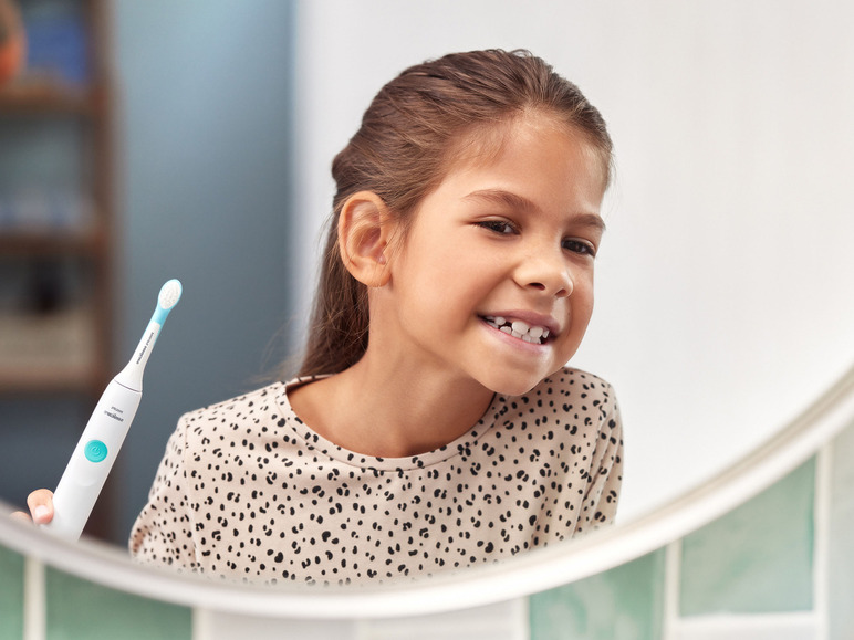 Une jeune fille tient une brosse à dents électrique Philips Sonicare devant le miroir.