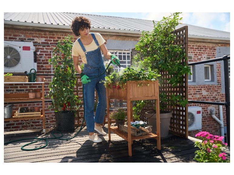 Une personne arrosant des fraisiers dans une jardinière surélevée en bois sur une terrasse sur le toit.