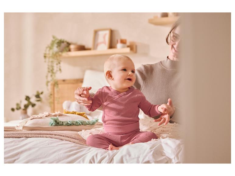 Bébé en vêtements roses assis sur un lit avec un adulte.