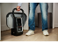 Personne tenant un défroisseur vapeur portable avec écran numérique, vêtue d'un jean et de baskets.