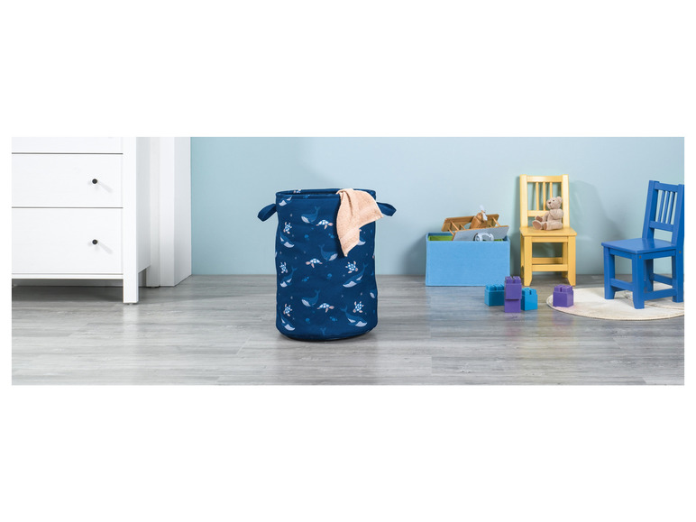 Un panier à linge bleu avec un motif de baleines et de tortues, deux chaises et des blocs dans une chambre d'enfant.