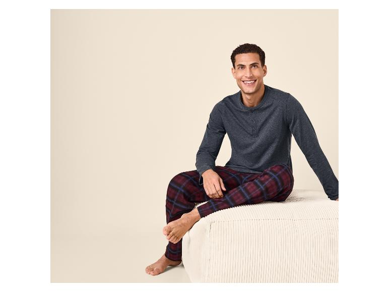 Homme souriant en pyjama à carreaux bordeaux et haut gris, assis sur un pouf.