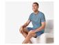 Homme souriant en t-shirt et short bleus, assis sur une chaise blanche.