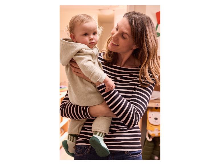 Une mère tient un bébé vêtu d'une combinaison beige clair.