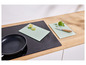 Deux planches à découper en verre avec un motif de feuilles, un couteau et une poêle sur une plaque de cuisson à induction.