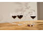 Verres à vin rouge, certains remplis, sur une table en bois avec ombres et raisins.