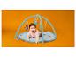 Bébé souriant sur un tapis d'éveil avec des jouets suspendus, fond orange.