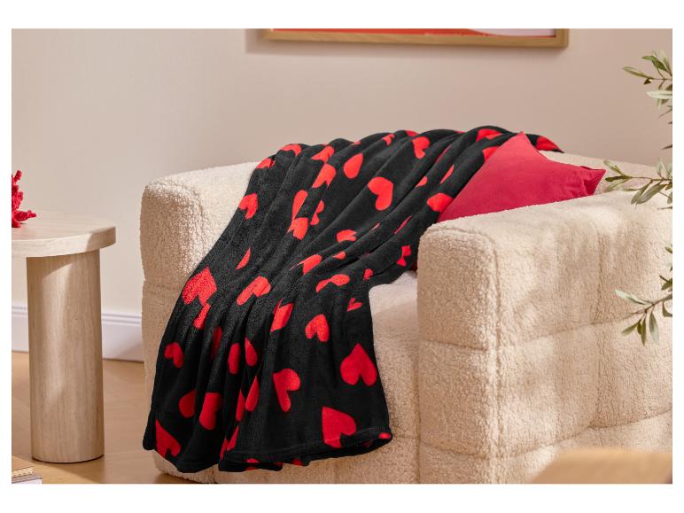 Plaid noir à cœurs rouges sur un fauteuil crème avec un coussin rouge.
