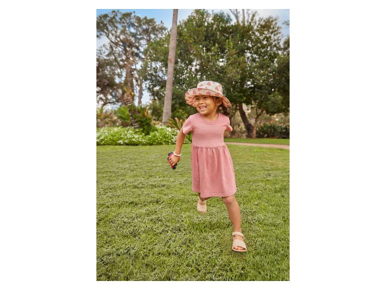 Fille joyeuse en robe rose et chapeau de soleil à cœurs courant sur l'herbe.