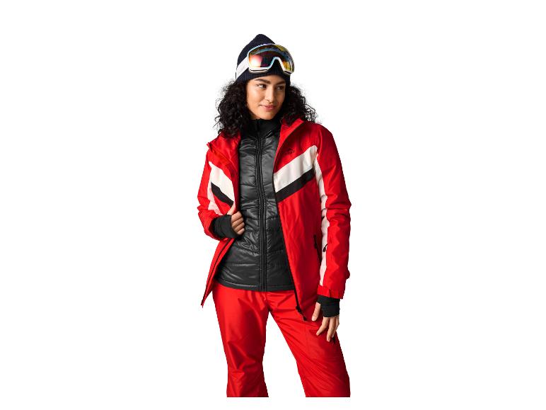 Femme en veste et pantalon de ski rouges et noirs avec masque de ski et bonnet.