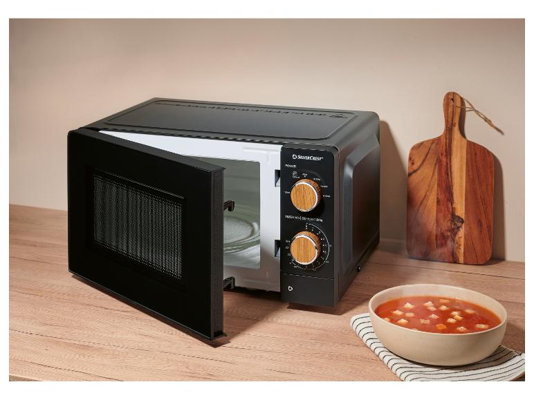 Micro-ondes noir avec porte ouverte, à côté d'un bol de soupe tomate et d'une planche à découper en bois.