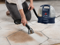 Une personne nettoie un tapis avec un nettoyeur de tapis portable, enlevant les taches.