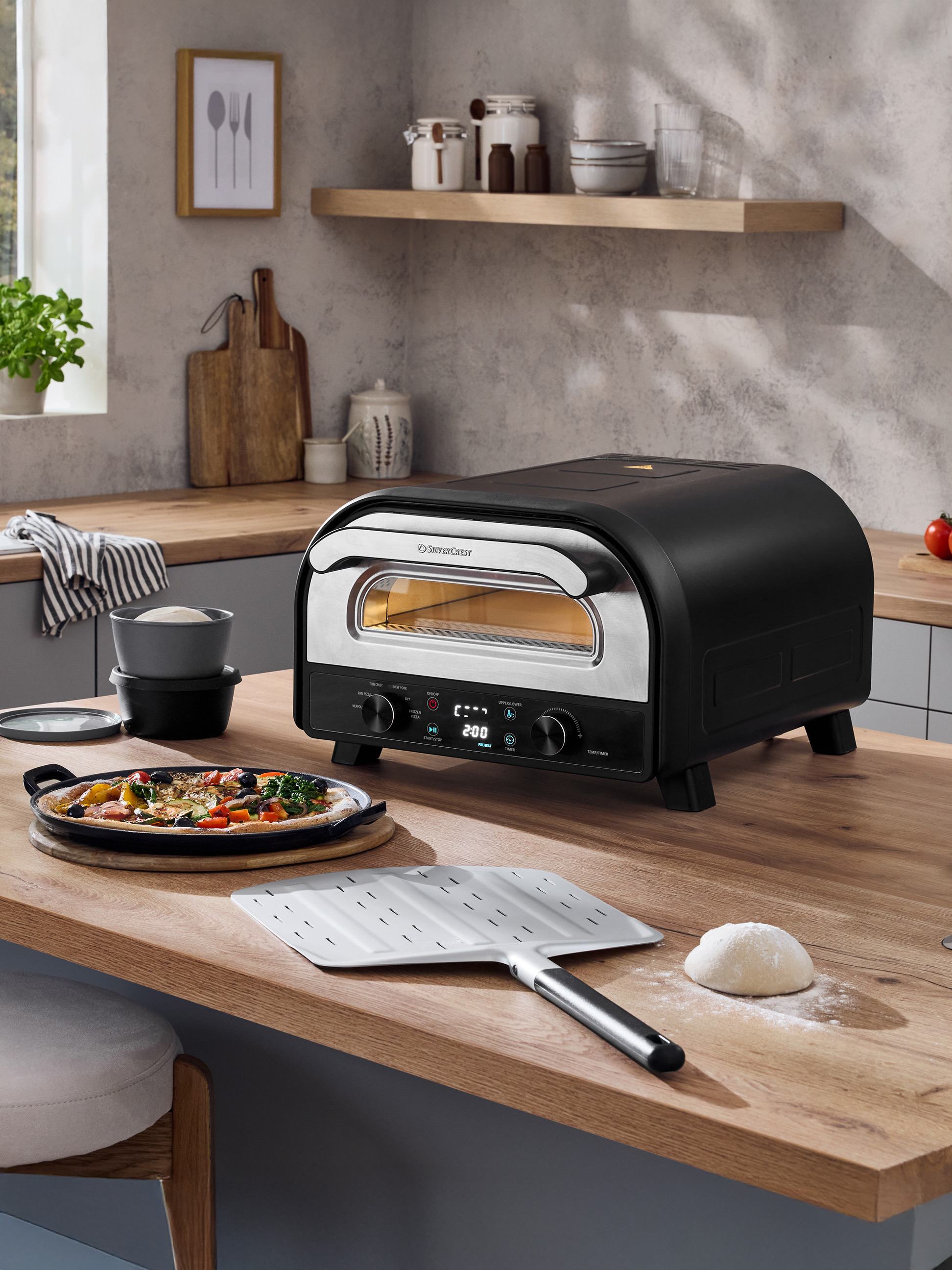 Four à pizza noir sur un comptoir en bois avec une pizza fraîchement préparée et de la pâte.